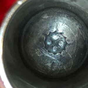 May include: Close-up view of a metallic object with a textured, spherical shape. The object appears to be inside a cylindrical container. The surface of the sphere has a pattern of cracks and a central, flower-like design.