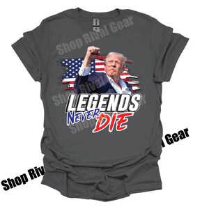 May include: A grey t-shirt featuring a graphic of a man in front of an American flag. The text "LEGENDS NEVER DIE" is printed in blue and red lettering.