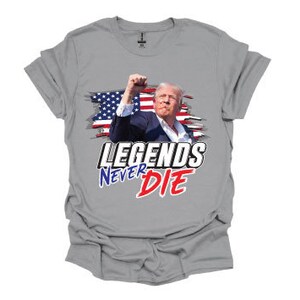 May include: A grey t-shirt featuring a graphic of a man in front of an American flag with the text "Legends Never Die" in red, white and blue.
