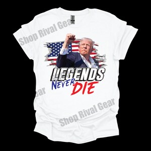 May include: White t-shirt featuring a graphic of a man in front of an American flag with the text "LEGENDS NEVER DIE" in bold, red, white and blue lettering.