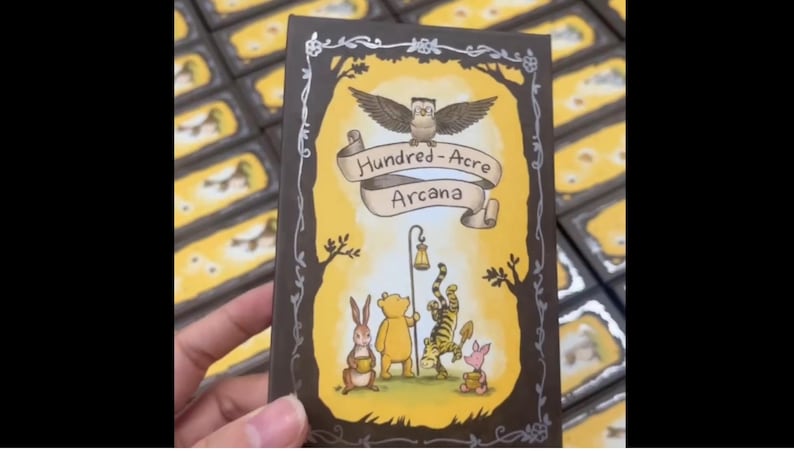 May include: A deck of cards featuring a whimsical illustration with the text "Hundred-Acre Arcana." The artwork includes an owl, Winnie the Pooh, Tigger, Piglet, and Rabbit. The card has a yellow background with a brown border.