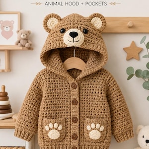 Puede incluir: Un suéter de ganchillo marrón para niños pequeños con capucha con orejas y cara de oso, cinco botones marrones en la parte delantera y dos bolsillos con diseños de huellas blancas. El texto dice: CROCHET TODDLER BEAR HOODED SWEATER ANIMAL HOOD + POCKETS.