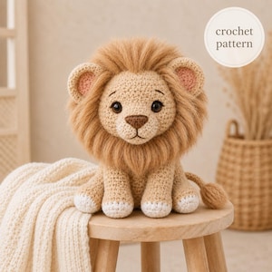 May include: A crochet lion toy with a tan body, white paws, and a fluffy brown mane. The lion has dark eyes, a brown nose, and pink inner ears. A circular white label in the upper right corner contains the text crochet pattern in brown letters.