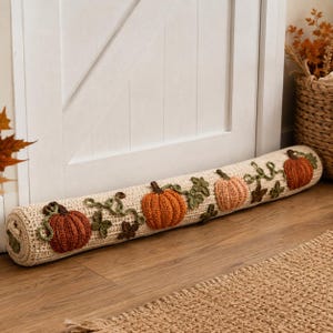 Peut inclure: Un boudin de porte cylindrique en crochet de couleur crème, orné de citrouilles en relief dans des tons orange foncé, orange vif et pêche clair, agrémenté de feuilles et de tiges en crochet vert sur toute la longueur.