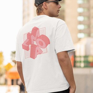 Op de afbeelding: Een wit T-shirt met korte mouwen en een roze driedimensionale afbeelding op de achterkant. De afbeelding toont de letters LMAO in een blokletterstijl, geplaatst tegen een vierkante achtergrond met een fijn stippenpatroon. Het shirt heeft een ronde hals.