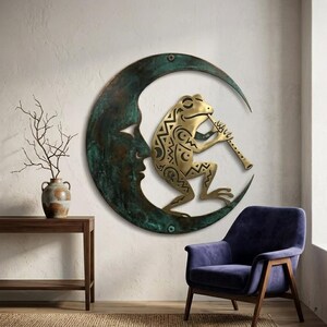 May include: A brass frog playing a flute, perched on a crescent moon with a face, mounted on a wall. The moon has a verdigris finish. A decorative wall art piece.