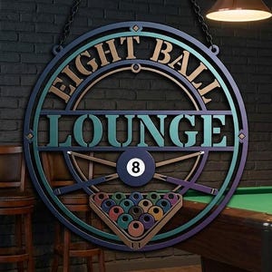 May include: A circular metal wall sign featuring the text EIGHT BALL LOUNGE in a bold font. The design includes a central graphic of a black eight ball, two crossed pool cues, and a triangular rack filled with colorful billiard balls.