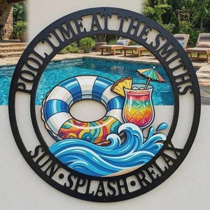 Puede incluir: Un letrero de pared circular de metal negro con el texto POOL TIME AT THE SMITHS y SUN SPLASH RELAX. El centro muestra una ilustración colorida de un flotador de piscina a rayas azules y blancas, un cóctel tropical con piña y olas.