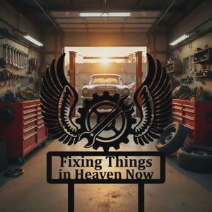 Puede incluir: Un letrero de metal negro con el texto "Fixing Things in Heaven Now" en un entorno de garaje. El letrero presenta un diseño de engranaje y llave inglesa con alas. Un coche clásico es visible en el fondo, junto con herramientas y equipos.