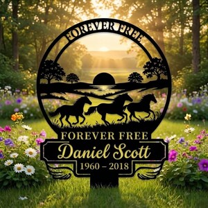 Puede incluir: Estaca de jardín conmemorativa de metal negro con las palabras "FOREVER FREE" y "Daniel Scott 1960-2018". La estaca presenta un diseño circular con caballos corriendo y una escena de puesta de sol. La estaca está colocada en un jardín con flores.