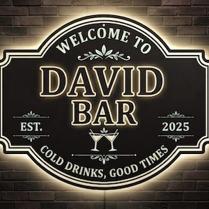 Puede incluir: Un letrero de pared rectangular negro con esquinas redondeadas y un borde LED blanco brillante. El texto dice WELCOME TO DAVID BAR, EST. 2025, y COLD DRINKS, GOOD TIMES. Un gráfico de dos copas de martini brindando está centrado bajo la palabra BAR.