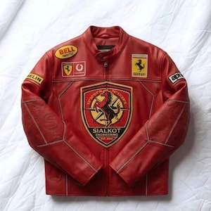 Könnte beinhalten: Eine rote Lederjacke mit einem zentralen schildförmigen Aufnäher, der ein Pferdemotiv und den Text SIALKOT ENGINEERING EST. 2006 zeigt. Die Jacke ist mit verschiedenen Rennsport-Aufnähern wie Ferrari-, Bell- und Michelin-Logos versehen.