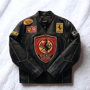 Könnte beinhalten: Schwarze Lederjacke mit mehreren Aufnähern, darunter ein Ferrari-Logo und ein schildförmiger Aufnäher mit einem Pferd. Die Jacke hat einen klassischen Motorradstil mit Reißverschluss und Stehkragen.