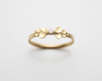 May include: A delicate gold ring with a small diamond set in the center, surrounded by a cluster of small, rounded gold shapes.