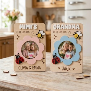 May include: Two wooden photo frames, one pink and one blue, each with a flower-shaped cutout. The frames feature the words "MIMI'S" and "GRANDMA" at the top, with "LITTLE LOVE BUG" below. Each frame has a photo of a person and a child.