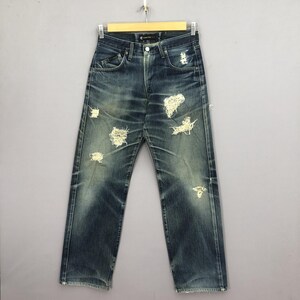 May include: Blue denim jeans with distressed details, including multiple rips and faded areas. The jeans are displayed on a hanger against a neutral background, showcasing a classic five-pocket design.