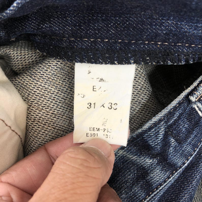 May include: Close-up of a pair of dark blue denim jeans. The tag reads "31 x 32". The jeans are folded, showing the inside lining and the tag with additional text.