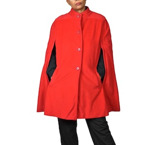 May include: A vibrant red cape coat with a stand-up collar and three matching buttons down the front. The coat features arm slits and two front pockets. The person in the image is wearing black pants and a black shirt under the cape.
