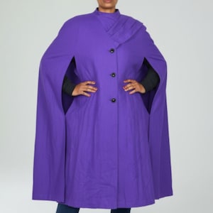 May include: A vibrant purple cape coat with a high collar and three black buttons. The coat features a unique design with arm openings and a draped shoulder detail. The garment is made of a solid color fabric.