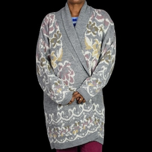 May include: A long-sleeved grey cardigan featuring a shawl collar and an intricate knit pattern in shades of white, muted pink, and pale yellow. The garment has a wrap-style front closure and ribbed cuffs, showcasing a floral and geometric design.