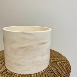 Peut inclure: Un pot de fleurs cylindrique blanc cassé avec un motif marbré brun rosé. Le pot a un bord lisse et arrondi et une base solide. Le récipient est conçu pour une utilisation intérieure ou extérieure et convient à diverses plantes.