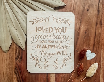 Puede incluir: Un letrero de madera con el texto "Loved you yesterday, love you still, always have, always will" grabado en él. El letrero está rodeado por un diseño floral decorativo.