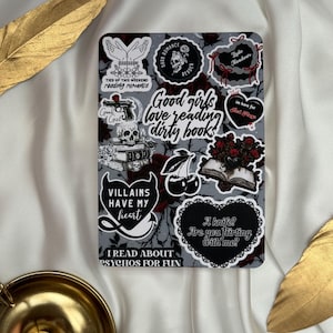 Könnte beinhalten: Ein rechteckiger Aufkleberbogen mit einem Dark-Romance-Thema, der Illustrationen von Totenköpfen, Büchern, Rosen, Kirschen und einer Handfeuerwaffe zeigt. Der zentrale Text lautet, Good girls love reading dirty books, umgeben von Sprüchen.