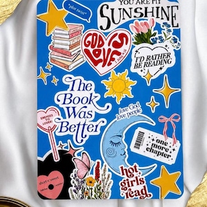 Può includere: Un foglio di adesivi rettangolare blu con varie illustrazioni e testi, tra cui una pila di libri, un cuore con il testo God's Love, una luna crescente, un biglietto con il testo one more chapter e frasi come The Book Was Better.