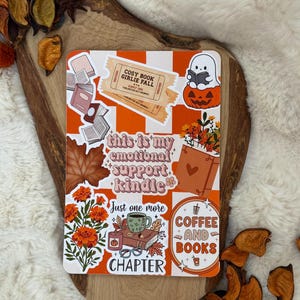 May include: A rectangular sticker sheet featuring an orange and white checkered background with various autumn-themed illustrations including a ghost on a pumpkin, books, leaves, flowers, and text reading "this is my emotional support kindle" and "COFFEE AND BOOKS".