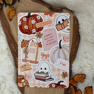 Op de afbeelding: Een rechthoekig stickervel met een lichtoranje ruitjesachtergrond, voorzien van diverse herfstafbeeldingen zoals pompoenen, geesten die boeken lezen, een tas met 'SWEATER WEATHER' en de tekst 'can't talk, i'm reading'.