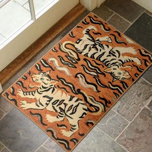 Peut inclure: Tapis rectangulaire orange avec un motif de tigre. Le tapis présente trois tigres crème avec des rayures noires, sur un fond de lignes ondulées orange et noires. Le tapis est placé près d'une porte.