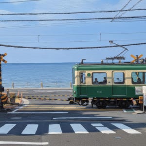 以下が含まれることがあります： 海岸沿いの踏切を通過する緑とクリーム色の電車。線路の横には黄色と黒の踏切警報機が設置されており、電車と横断歩道の背景には青い海が広がっている。