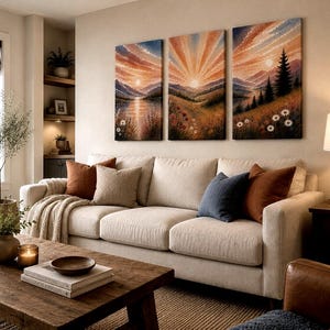 May include: A triptych wall art set featuring a continuous landscape painting of a sunrise over mountains, a lake, and a forest with wildflowers. The three rectangular canvases display warm orange, yellow, and blue hues across the sky.