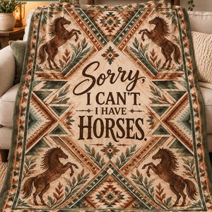Peut inclure: Un plaid vert sauge et crème orné de quatre chevaux bruns cabrés, de motifs géométriques et du texte "Sorry, I CAN'T. I HAVE HORSES." Le motif est disposé en losange avec des détails de feuilles.