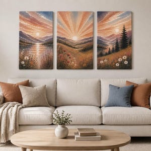 May include: A triptych wall art set featuring a landscape painting of a sunrise over mountains, a lake, and a meadow with wildflowers. The three rectangular canvases display a continuous scene with warm orange, pink, and blue sky tones.