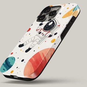 May include: A white smartphone case featuring a graphic illustration of an astronaut floating in space. The design includes colorful planets in shades of orange, teal, and red, along with small black and yellow dots scattered across the surface.