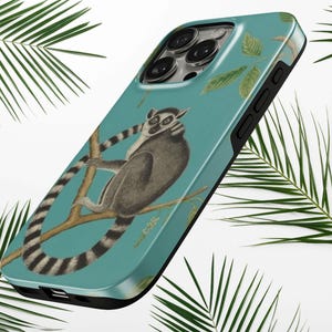 May include: A teal phone case featuring a detailed illustration of a ring-tailed lemur perched on a brown branch. The lemur has grey fur, a white face with dark eye patches, and a long, black-and-white striped tail. Green leaves are scattered.