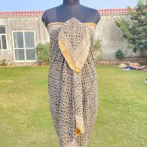 May include: A sarong featuring a dark brown and cream repeating floral pattern with a solid gold border. The fabric is draped over a mannequin torso, showcasing the intricate block-print style design and the contrasting hemline detail.