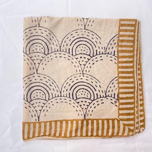 May include: A square textile featuring a beige base with a repeating pattern of dark blue concentric semicircles and dashed lines. The fabric is bordered by a wide mustard yellow band with a vertical stripe pattern along two adjacent edges.