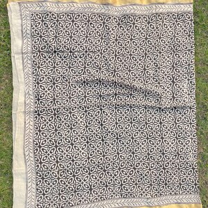 May include: A rectangular textile featuring a dark brown repeating geometric pattern on a cream background. The fabric is bordered by a thin, dark brown line and a wider, solid gold-coloured edge, creating a distinct frame around the central design.