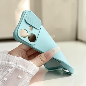 Op de afbeelding: Een lichtblauwe telefoonhoes met een schuifbare camerahoes. De hoes heeft uitsparingen voor de camera en andere functies van de telefoon. De hoes wordt in de hand van een persoon gehouden.
