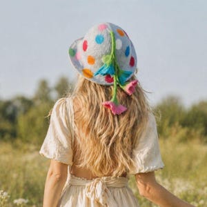 May include: A light grey hat with colourful polka dots and a floral design. The hat features a wide brim and is adorned with orange, pink, blue, and green accents. A unique fashion accessory.
