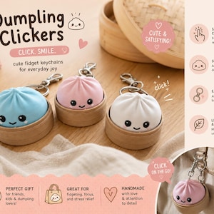 May include: Three Dumpling Clickers fidget keychains in blue, pink, and white, each featuring a smiling face and resting in a small wooden steamer basket. The keychains include metal lobster clasps for attachment to bags or keys.