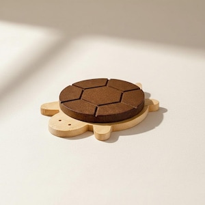 May include: A wooden turtle-shaped coaster with a dark brown, segmented top resembling a soccer ball. The base is light-colored wood, and the design includes small, round eye details. The coaster is designed for placing drinks.