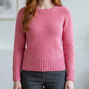May include: A long-sleeved, crew-neck jumper in a solid pink colour, featuring a textured crochet stitch pattern throughout the body and sleeves, with ribbed detailing at the neckline, cuffs, and hem, paired with dark grey trousers.