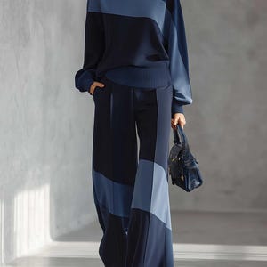 Puede incluir: Un conjunto de suéter de manga larga y pantalones de pierna ancha con un diseño de bloques de color en tonos azul marino y azul claro. El suéter tiene cuello redondo y puños acanalados, mientras que los pantalones incluyen bolsillos laterales.