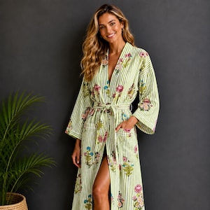Peut inclure: Une robe de chambre longue arborant un motif à rayures verticales vert clair et blanc avec un imprimé floral coloré. Le vêtement comprend des manches longues, une ceinture à nouer et deux poches avant avec des bordures blanches.