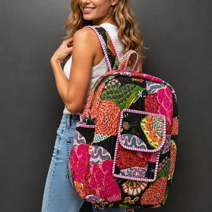 Könnte beinhalten: Ein gesteppter Rucksack mit schwarzer Basis und einem lebendigen, mehrfarbigen Blumen- und Abstraktmuster in Rosa-, Orange-, Grün- und Gelbtönen. Die Tasche verfügt über eine Vordertasche mit Klappe und einen rosa-weiß karierten Rand.