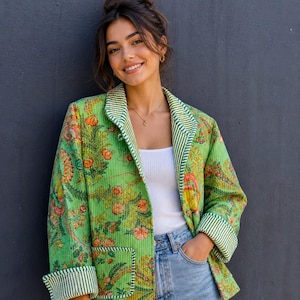 May include: A quilted jacket in a vibrant green hue featuring a multi-coloured floral print. The garment includes long sleeves with white and green striped cuffs, a matching striped lapel, and two front patch pockets with striped trim detailing.