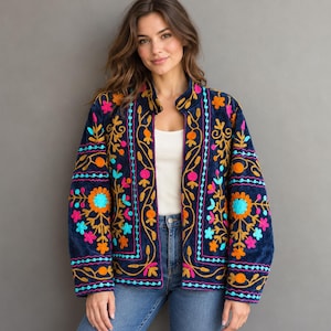 May include: A navy blue velvet jacket featuring vibrant, multi-colored floral embroidery in shades of bright orange, hot pink, and turquoise. The jacket has a stand-up collar, long sleeves, and a straight hem, worn over a white top and blue jeans.